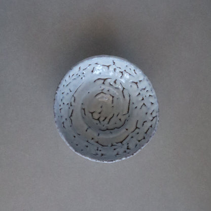 Top-down view of a handcrafted Shino chawan with a white glaze featuring a pinhole texture, displayed on a grey surface.