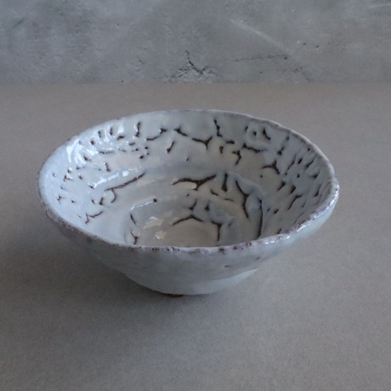 A Shino chawan tea bowl with a textured white glaze and orange-brown fire color accents, handcrafted in a traditional Japanese style, displayed on a grey backdrop.