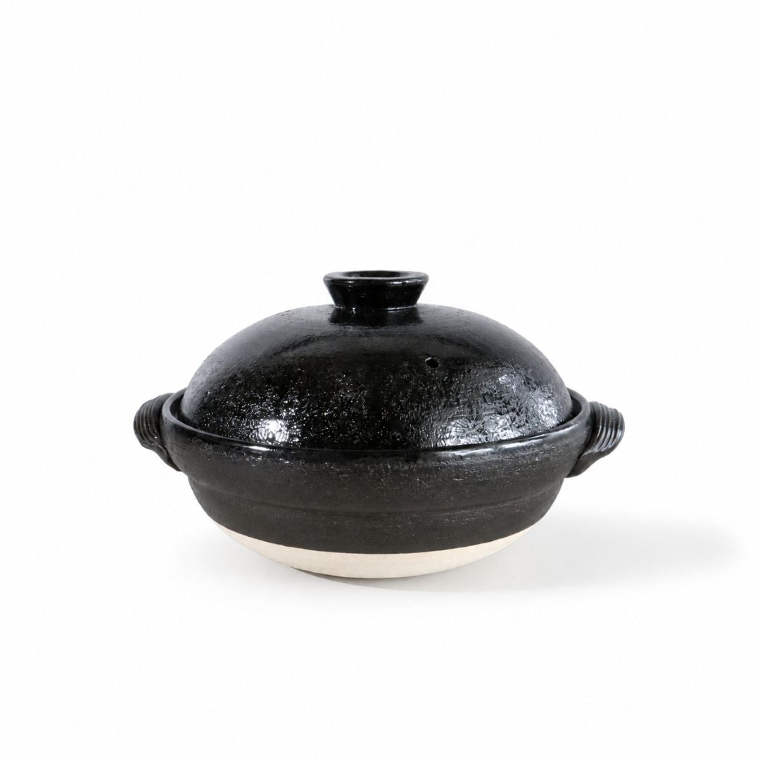 A black ceramic lidded pot with side handles and a textured glaze, set against a plain white background.