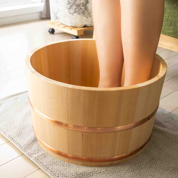 side view of a woman soaking her feet in a wood soaking bath placed on a grey carpet in a room