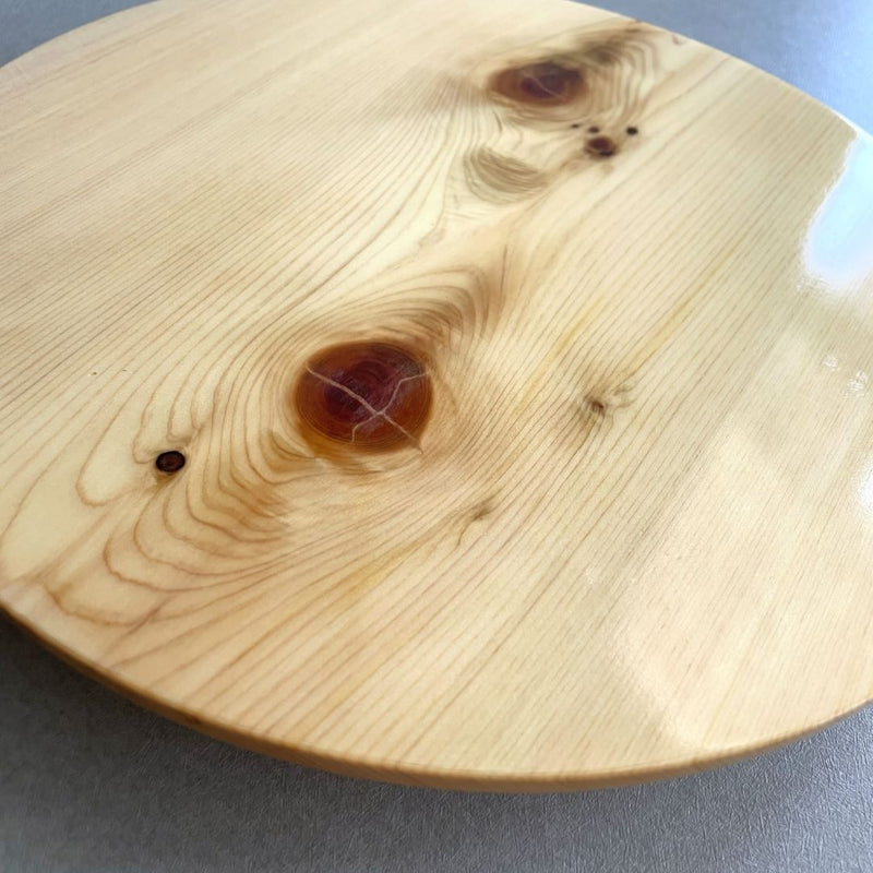 Close-up of a round wooden sushi plate against a grey wall background.