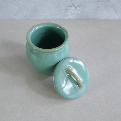 Handmade Japanese ceramic jar with a retro green glaze, shown with its lid removed. This Mashiko Ware jar has a smooth, glossy finish and a curved shape, perfect for storing spices, tea, or small keepsakes.