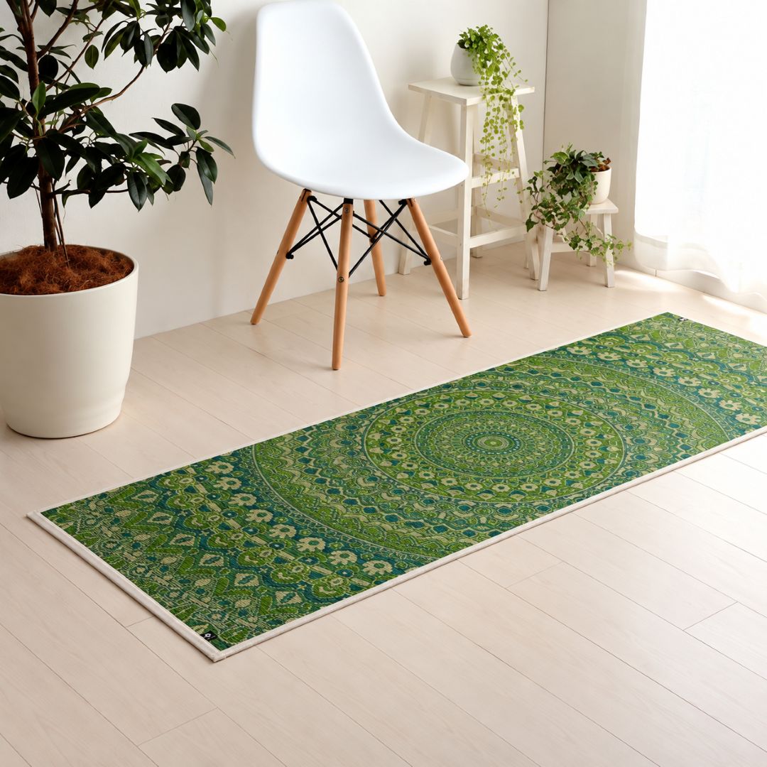 A green runner rug with a detailed mandala pattern, styled on a light wood floor in a bright, modern room with a white chair and potted plants.