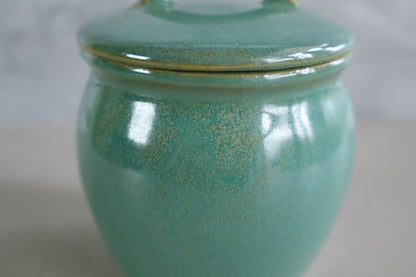 Close-up of a handmade Japanese ceramic jar with a retro green glaze, highlighting its smooth, glossy finish and subtle speckled texture.