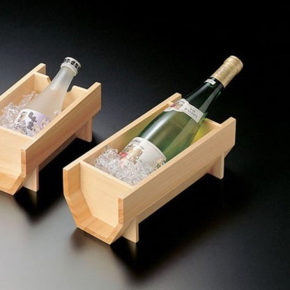 One bottle of wine and one sake bottle, each in wooden chilling buckets with ice, centered in a black room.