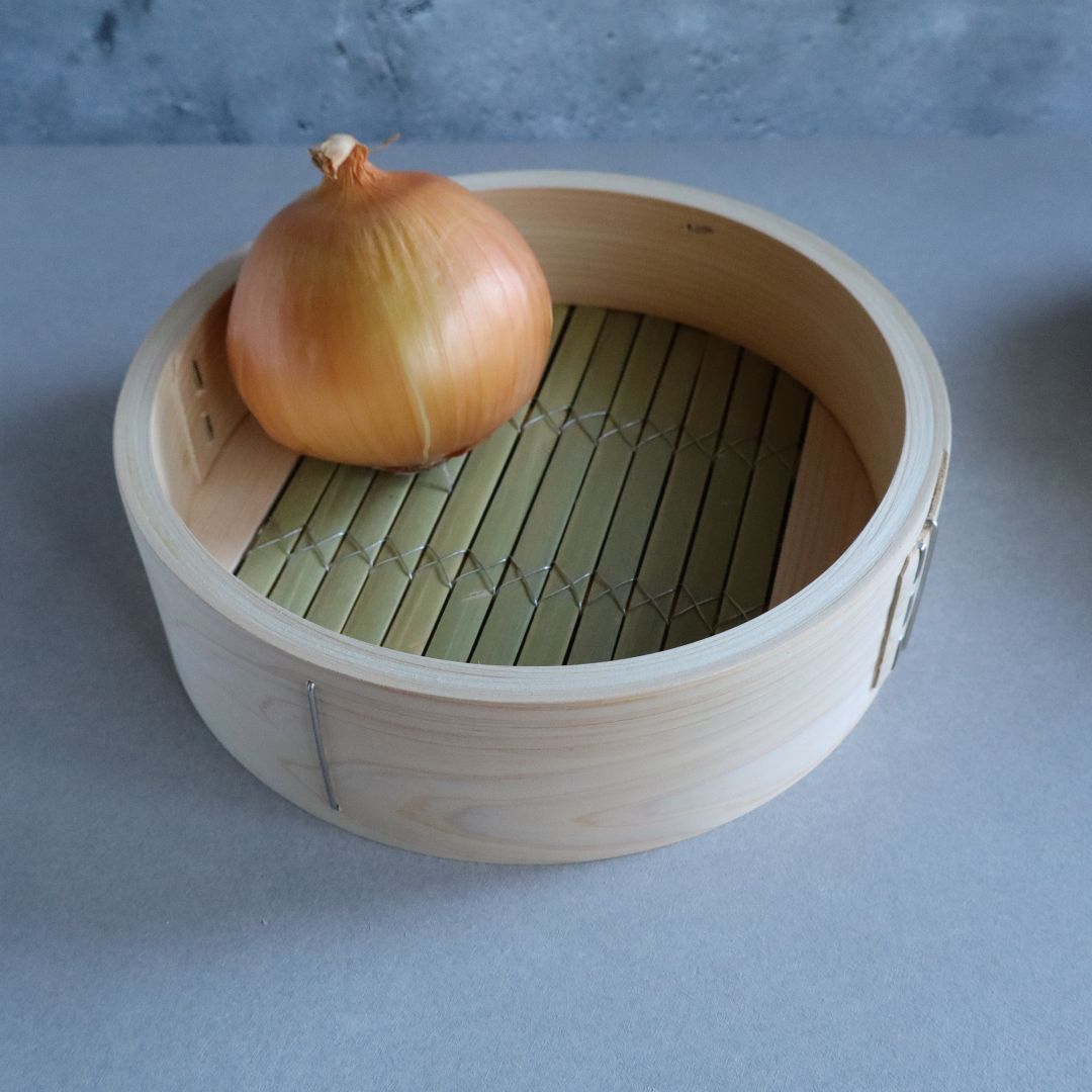 Wooden steamer basket with a single onion on a gray background