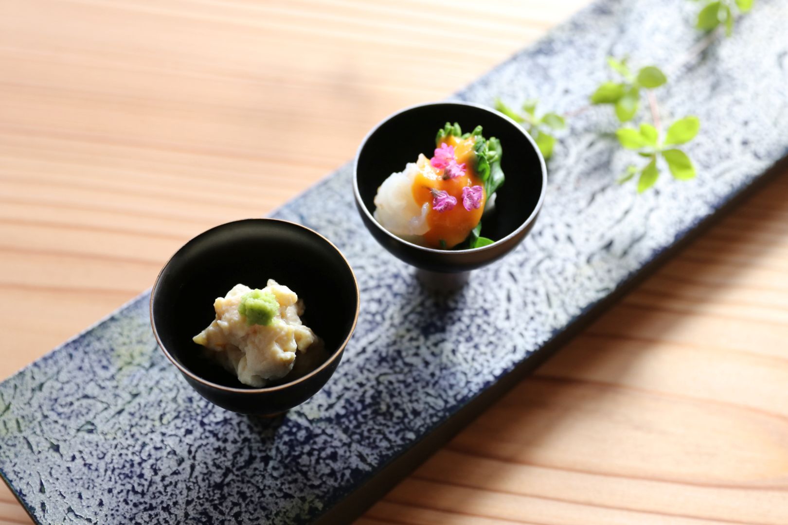 Two small black bowls with food on a decorative mat on a wooden surface
