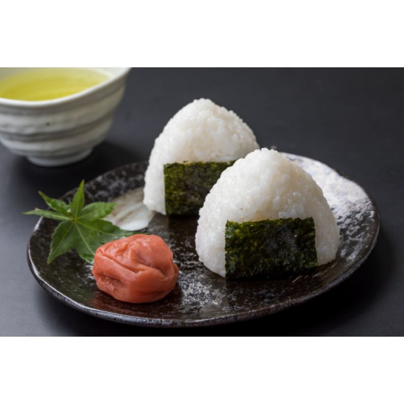 Two rice balls on a black plate with a white ceramic tea bowl next to it.