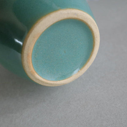 Close-up of the bottom of a handmade Japanese ceramic jar, featuring a smooth retro green glaze with an unglazed rim highlighting its natural clay texture.