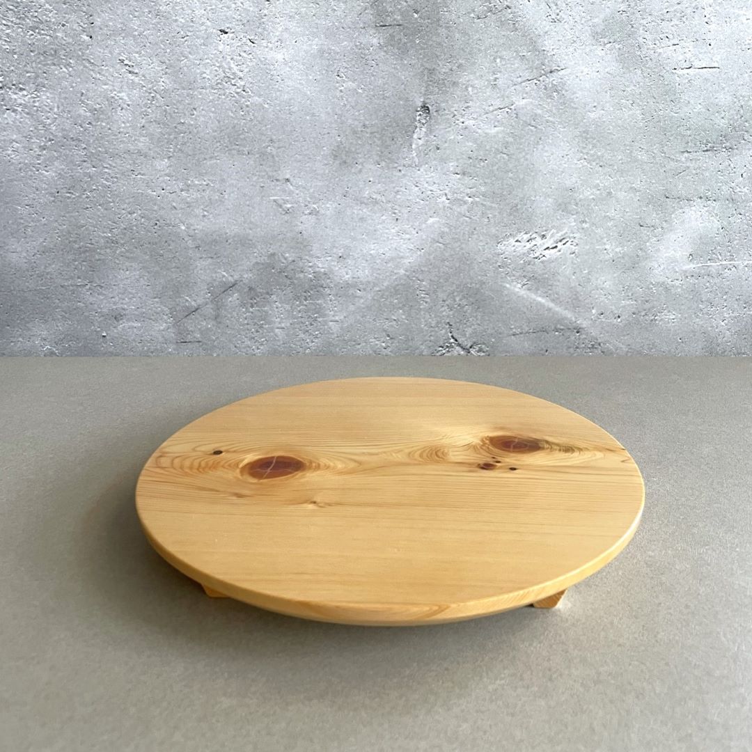 Front view of a round wooden sushi plate against a grey wall background.