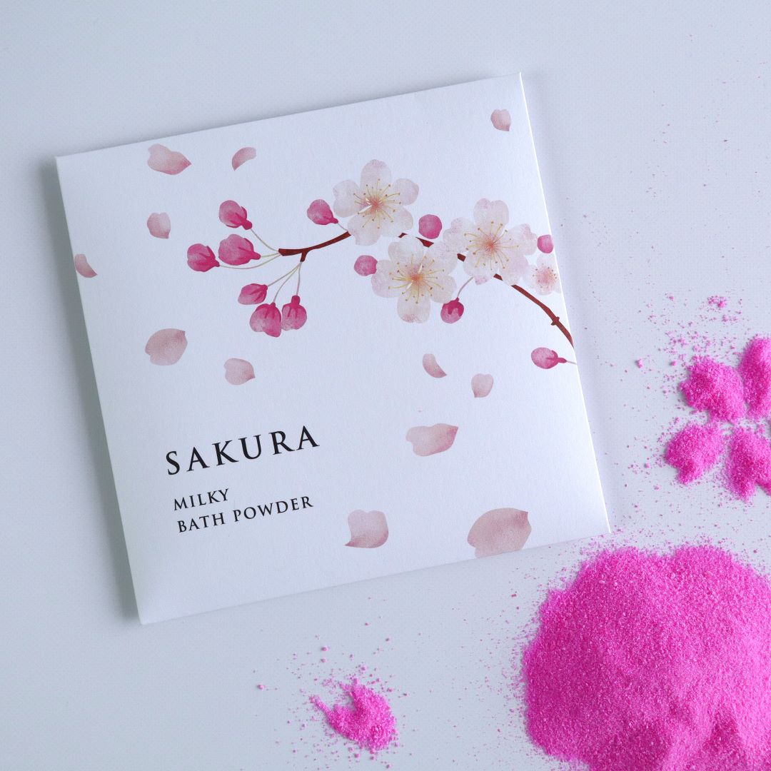 Sakura Milky Bath Powder pack next to vibrant pink bath powder on a white background.
