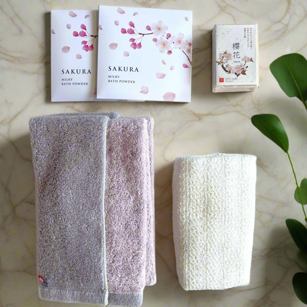 Japanese Sakura Bath Gift Set with an Imabari towel, natural wooden body brush, Sakura soap, and milky bath powder, elegantly arranged on a marble surface for a luxurious spa-like experience.