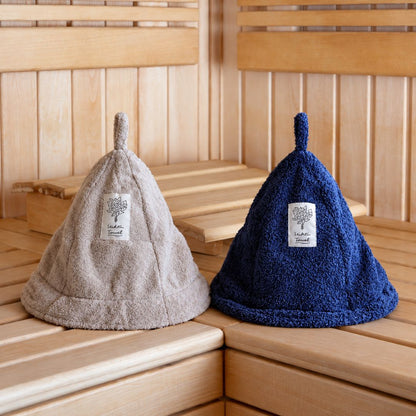 Two textured knit sauna hats, one in beige and one in navy blue, displayed on wooden sauna benches.
