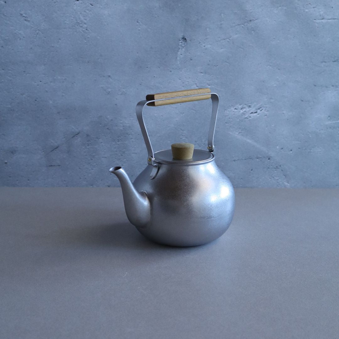 Silver teapot with a wooden handle on a gray surface and background