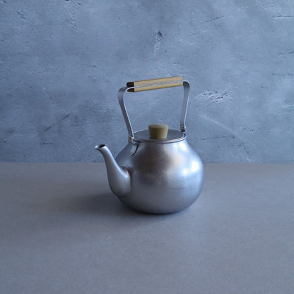 Silver teapot with a wooden handle on a gray surface and background