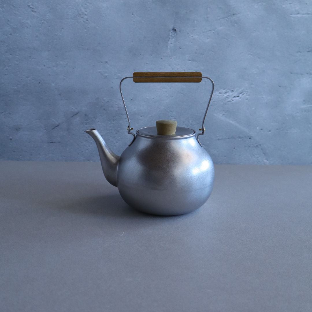 Silver teapot with a wooden handle on a gray surface and blue background