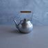 Silver teapot with a wooden handle on a gray surface and blue background