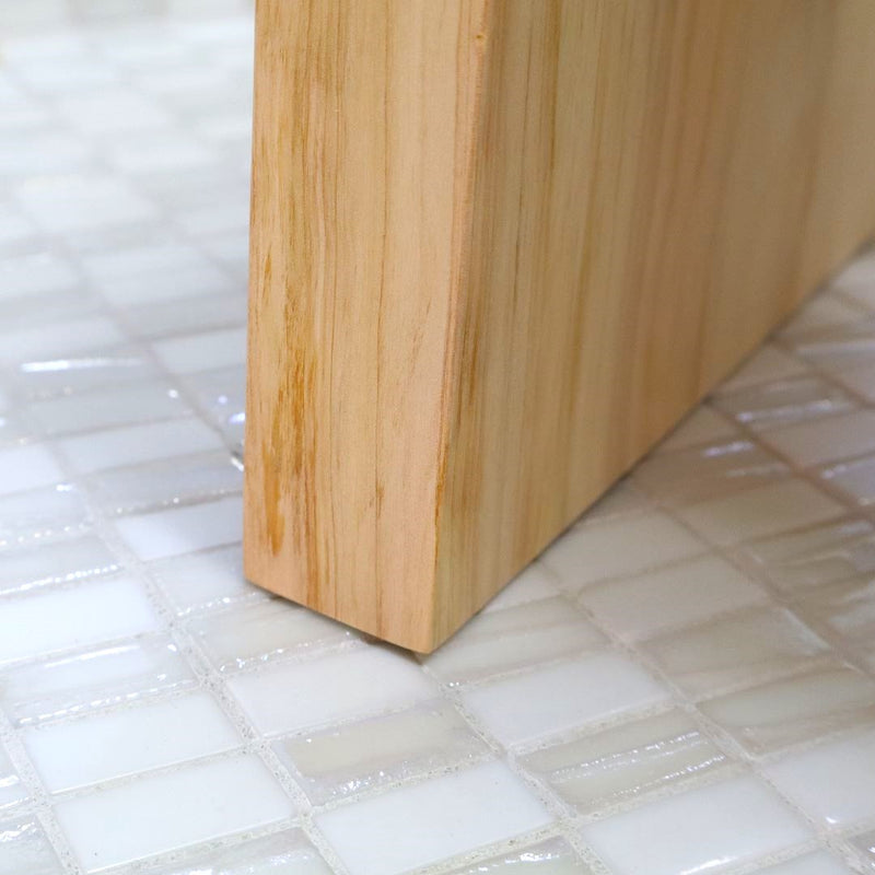 Close-up of a corner of a Hinoki wood bath chair on glossy white mosaic tiles, highlighting the chair& natural wood grain and craftsmanship.