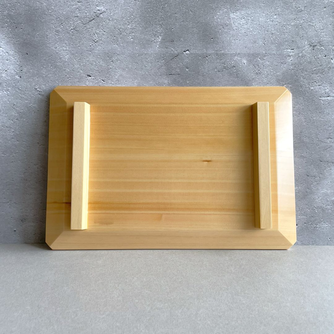 A simple wooden tray with raised edges on a textured grey concrete surface, showcasing the tray&