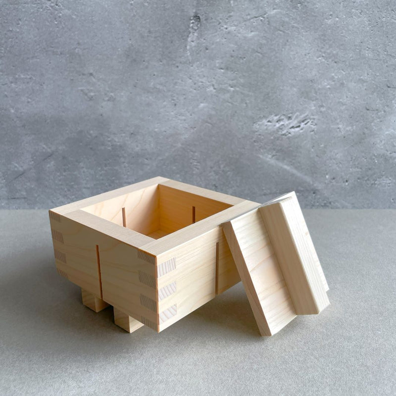 a wooden sushi square with a lid side to the box in a grey room.