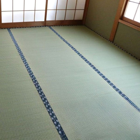 A traditional Japanese room featuring neatly arranged tatami mats with a decorative blue border. The room has shoji sliding doors and wooden accents, creating a serene and authentic Japanese aesthetic.