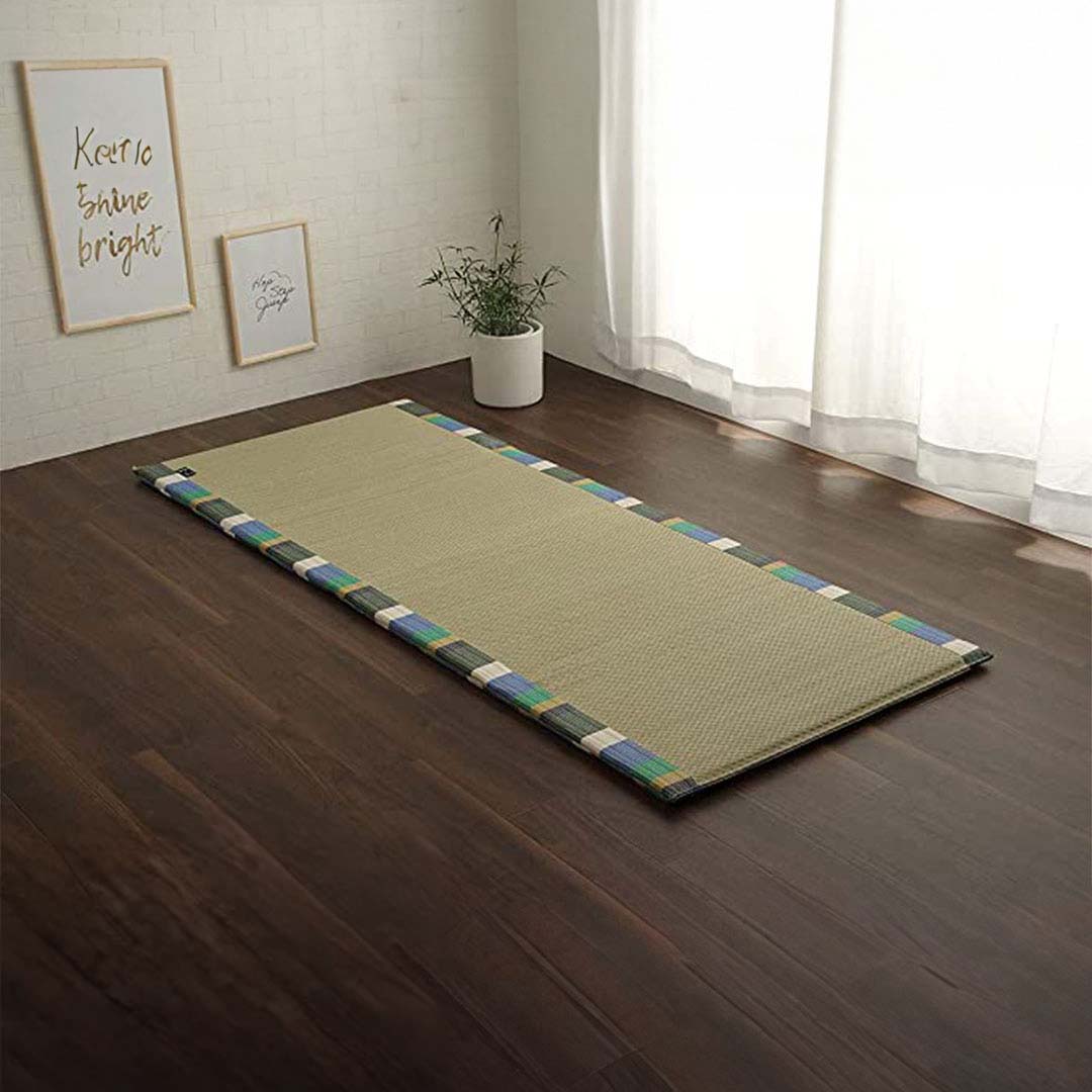 Green tatami mat on a wooden floor with framed pictures and a plant in the background.