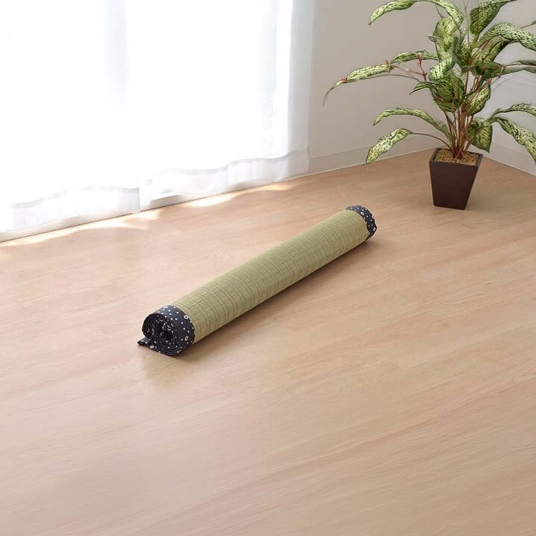 Rolled-up green mat on a wooden floor with a plant in the background