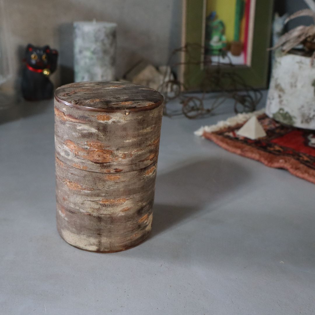 A cylindrical tea caddy made of natural wild cherry bark with a marbled pattern, displayed on a flat surface.