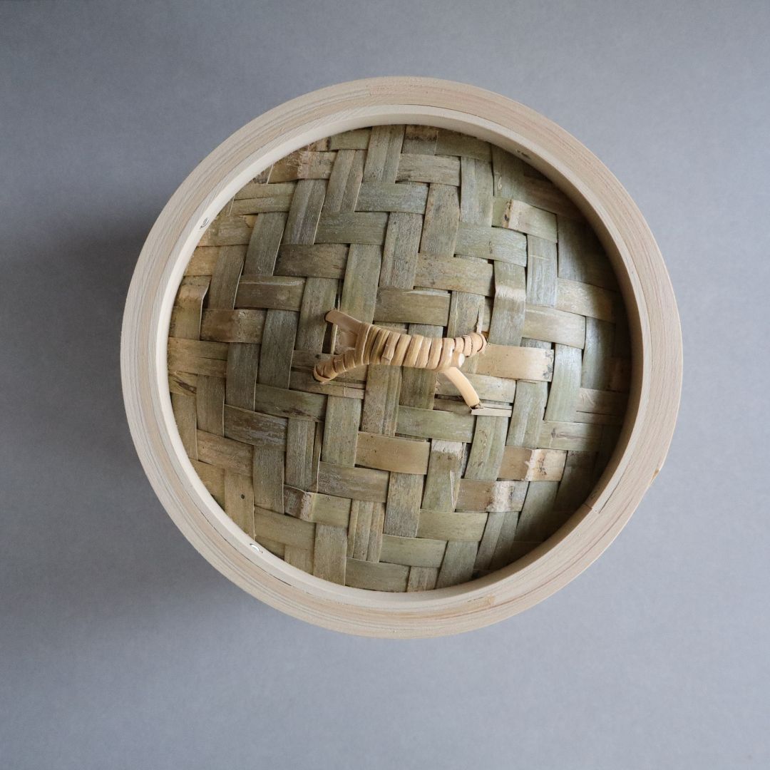 Round woven basket with a small wooden tiger figurine on a gray background