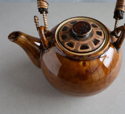 Close-up view of the interior of a handmade Japanese ceramic teapot, showing the built-in ceramic strainer with multiple small holes, designed for brewing loose-leaf tea. The teapot's glossy brown glaze and traditional craftsmanship are visible.