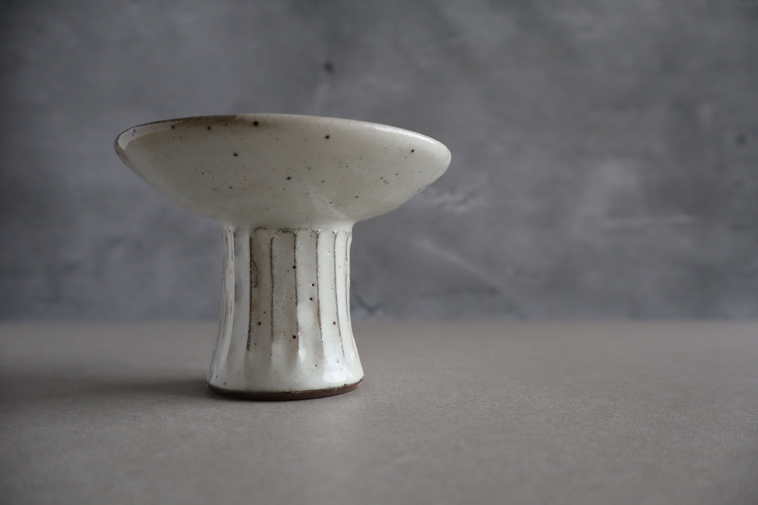 White ceramic pedestal dish with brown accents on a gray background