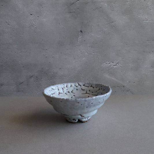 A Shino chawan tea bowl with a textured white glaze and orange-brown fire color accents, handcrafted in a traditional Japanese style, displayed on a grey backdrop.