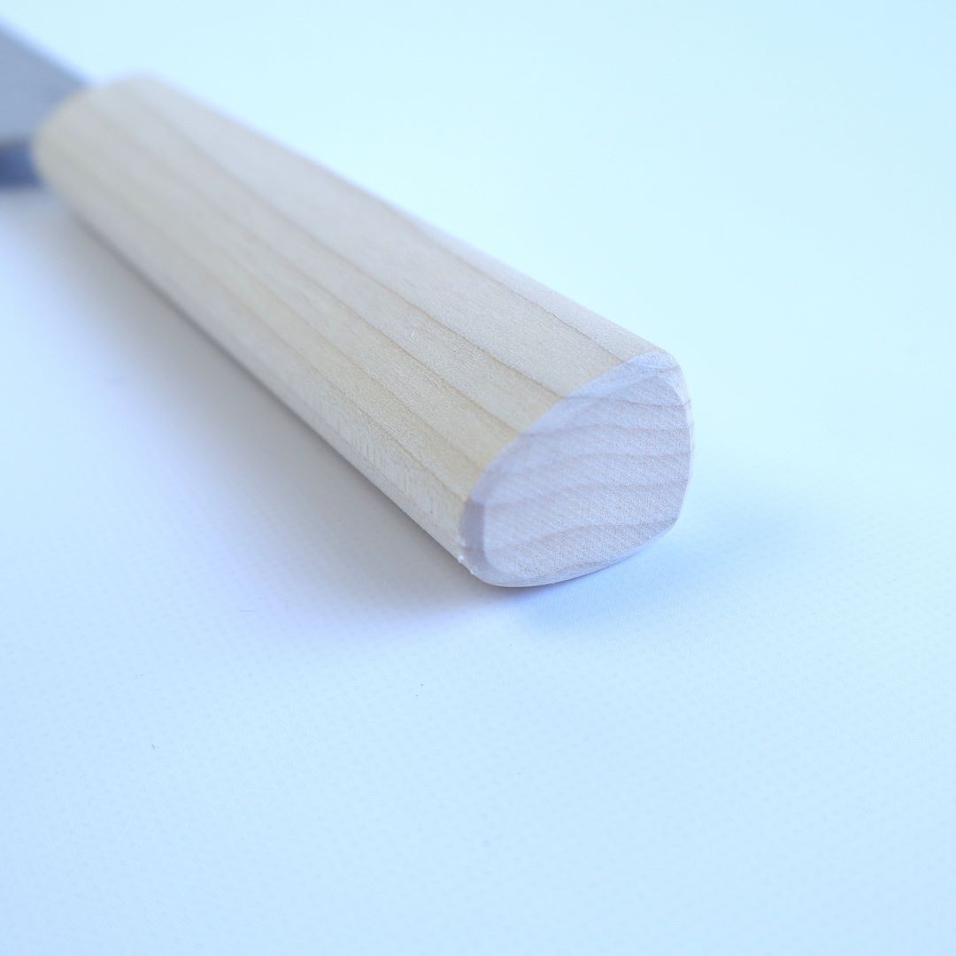 A close-up image of the end of a pale, natural wood knife handle, showing off the fine grain and smooth, unvarnished surface, with the handle resting diagonally across a soft white background. The craftsmanship is evident in the precise, rounded end and the subtle textural details of the wood.