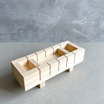 A rectangluar wooden sushi mold to make square sushi on a grey table in front of grey wall