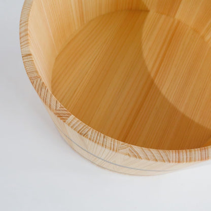 A close-up of a light natural wood bath bucket with visible grain and a small metal band around the rim, photographed on a white background.