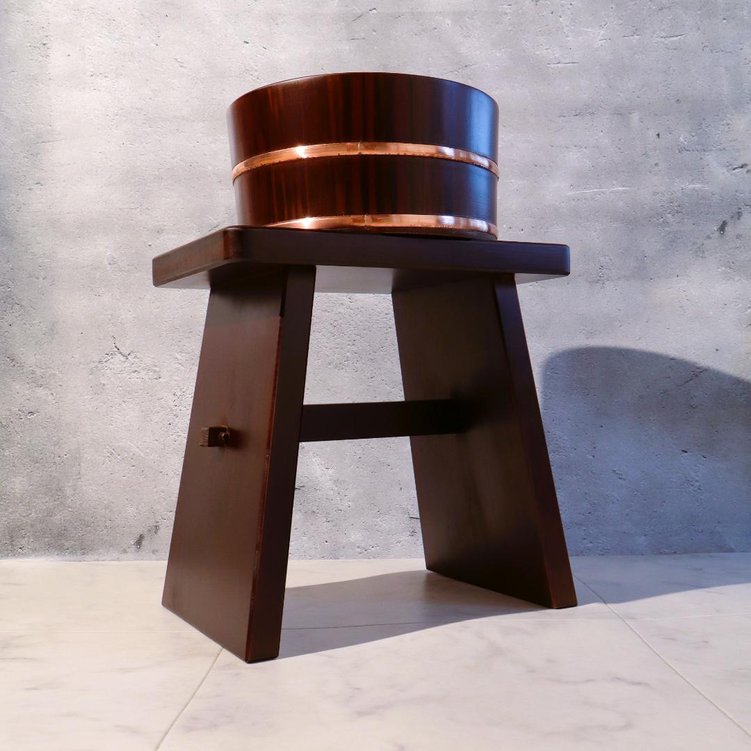 Wooden stool with a metallic top against a concrete wall.