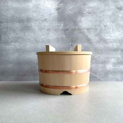 Front view of a wooden rice bucket placed on a light brown table in a grey room.