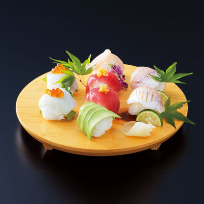 Top view of a round wooden sushi plate displaying colorful sashimi against a black wall background.