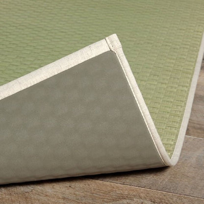 Close-up of a Japanese rush grass tatami mat with a folded corner, revealing its non-slip TPE rubber backing. The mat features a natural green checkered pattern with a beige fabric border, highlighting its durable and high-quality craftsmanship.