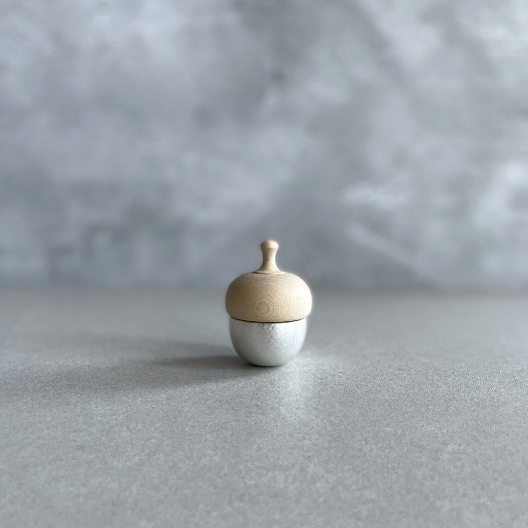 A small acorn-shaped healing bell with a silver base and a wooden top, placed on a smooth surface against a soft, neutral background.