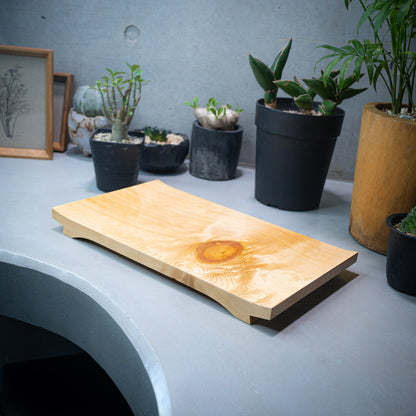On a grey kitchen counter, a wooden tray for sushi is prominently displayed. In the background, green plants and two cacti are visible, adding a natural touch to the scene.