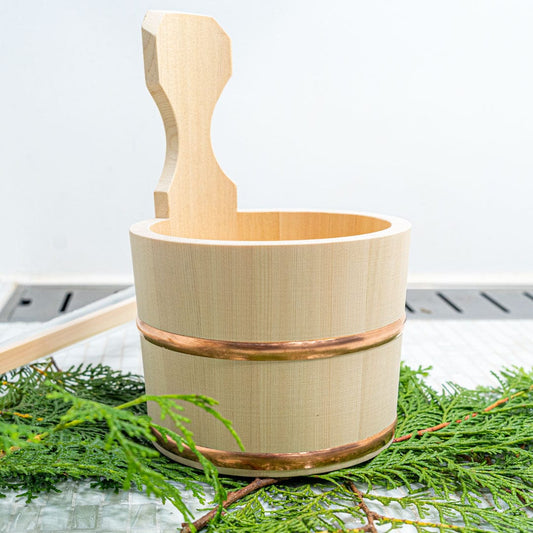 A Japanese wooden bath bucket with handle on a pine branch inside a white bathroom floor
