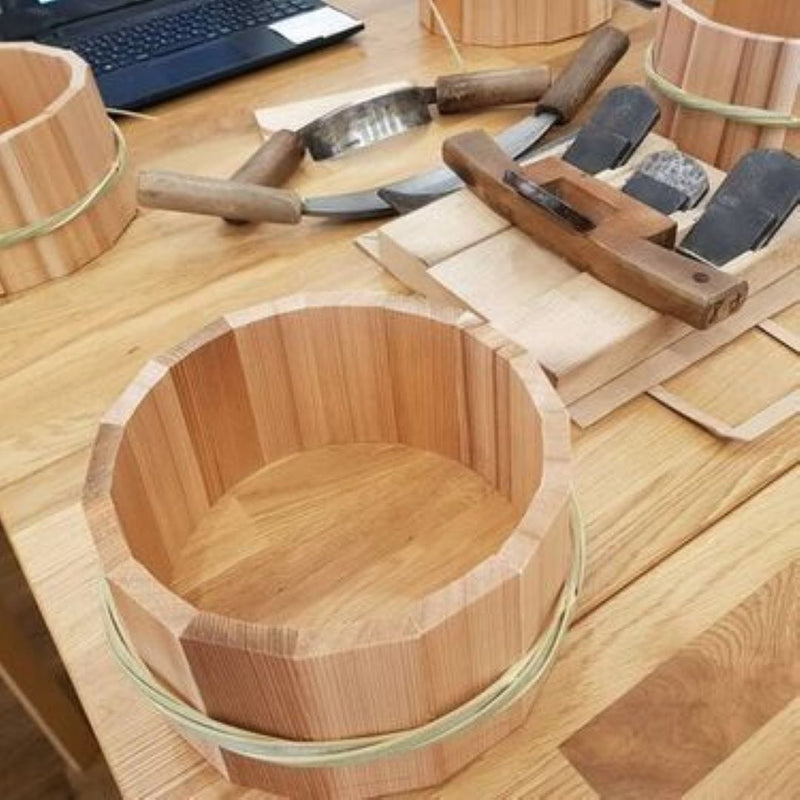 A wooden table where one bucket is being made and different carpentry tools and three bucket in background and a computer