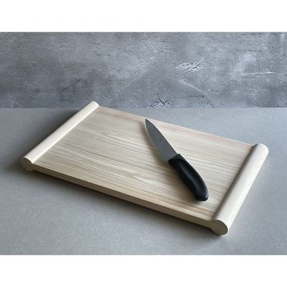 wooden cutting board a grey surface with a black knife on one side