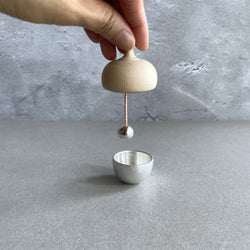 Hand holding a wooden bell over a grey iron singing bell, placed in the center of a grey room.