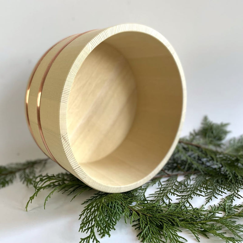 wooden bath bucket laid on a its side on pine branch in a white background