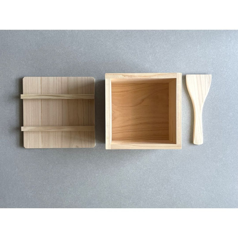 open rice box made of wood next to its lid and kitchen tool