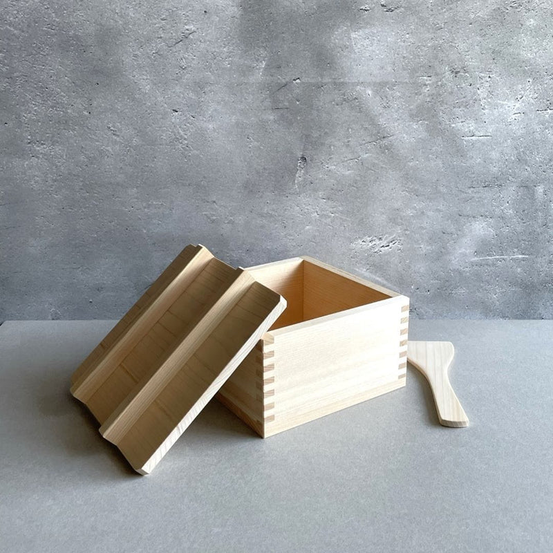 wooden rice container with open lid on side of the box and kitchen tool next to it