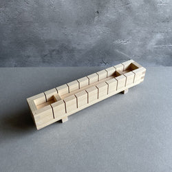 A wooden sushi mold sitting on a grey surface, with a grey wall in the background.