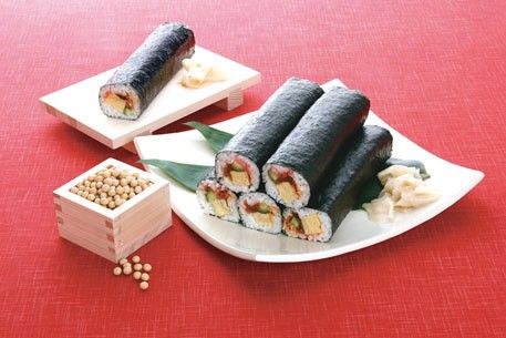 one white ceramic plate with five roll maki on it and one roll maki on a wooden plate red carpet